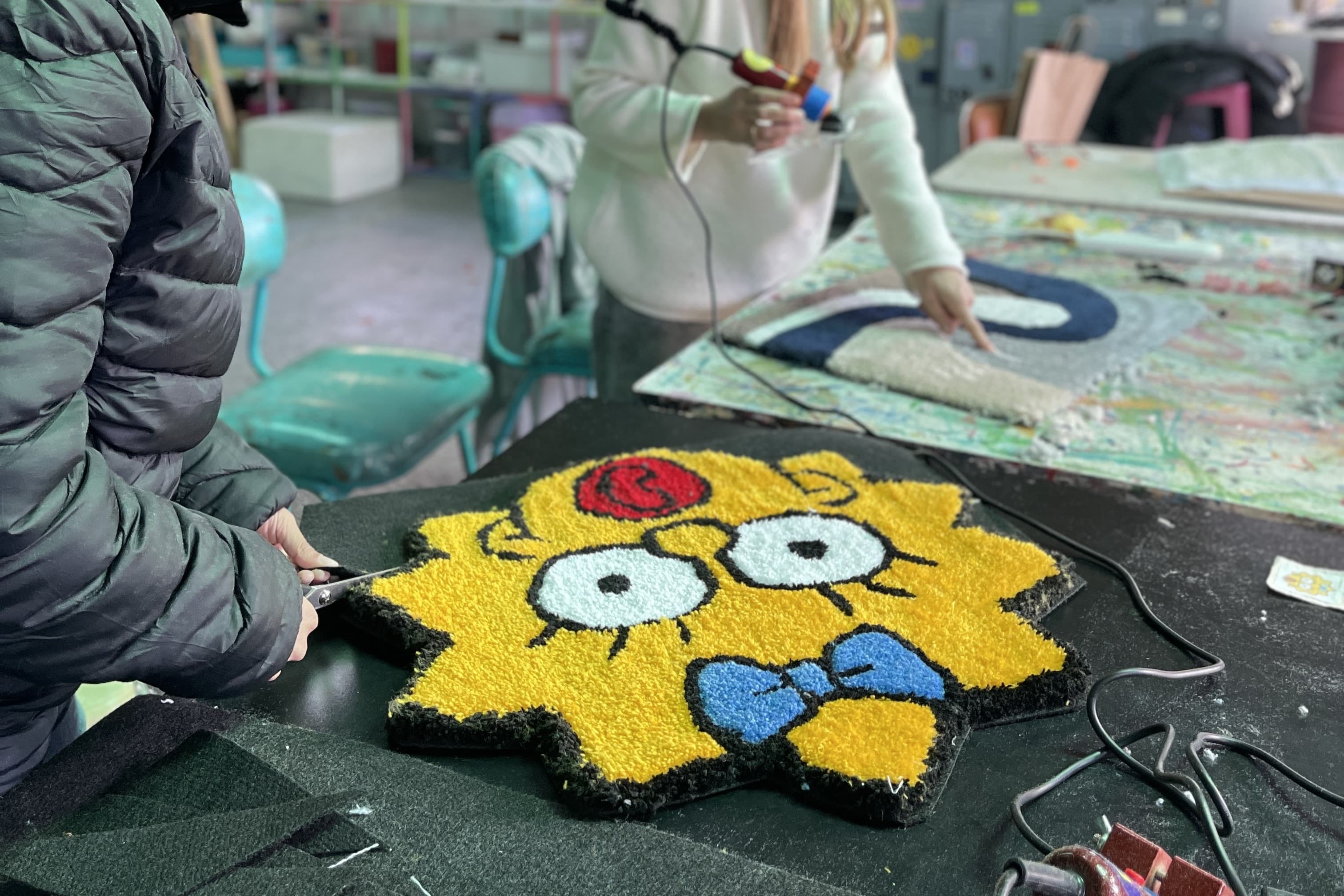 Alumna recortando alfombra de tufting con diseño de Maggie Simpson en taller Maxitufting